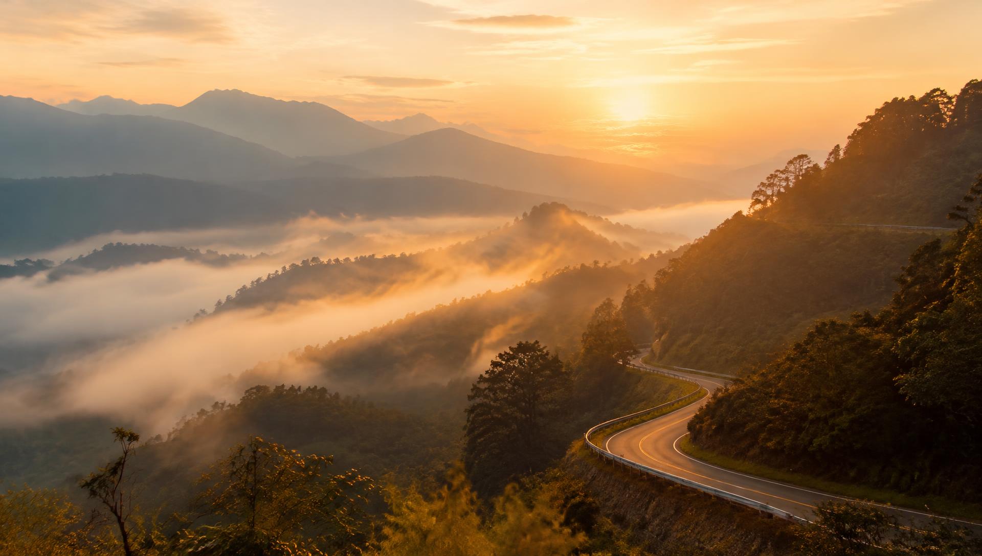 Misty mountain valley at sunrise with a winding road